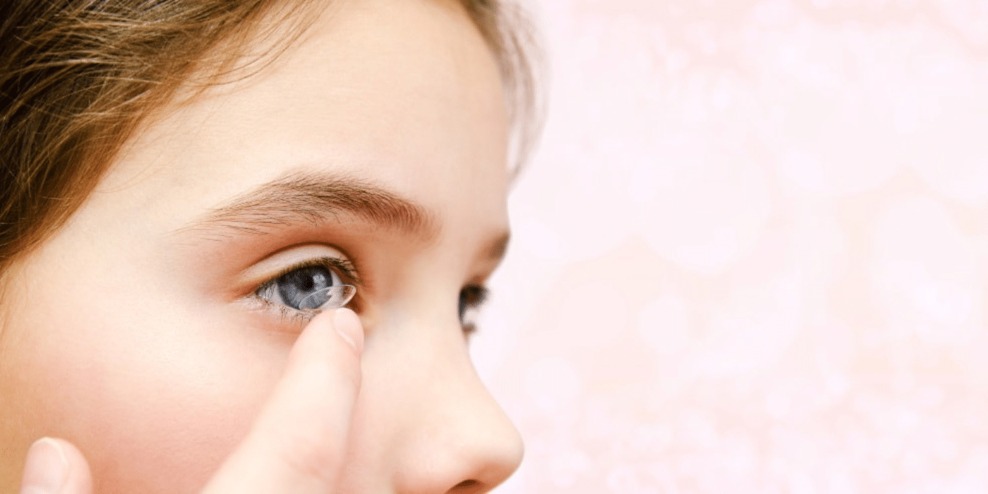 Young girl inserting contact lens into eye