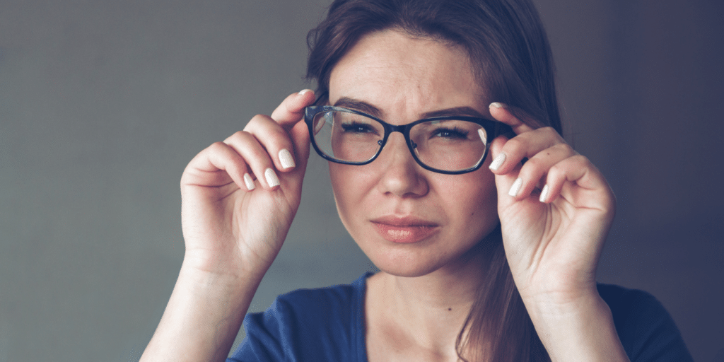Woman holding glasses squinting due to blurry vision