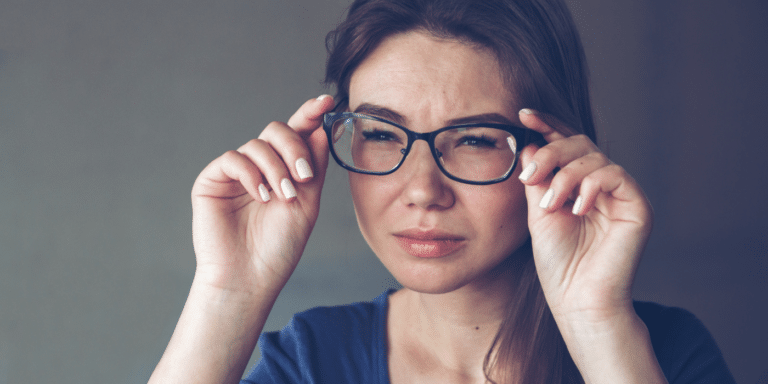 Woman holding glasses squinting due to blurry vision